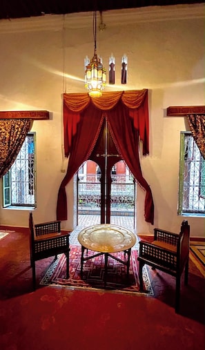 A room with a round table, two chairs, a hanging light fixture, and a view through an arched doorway.