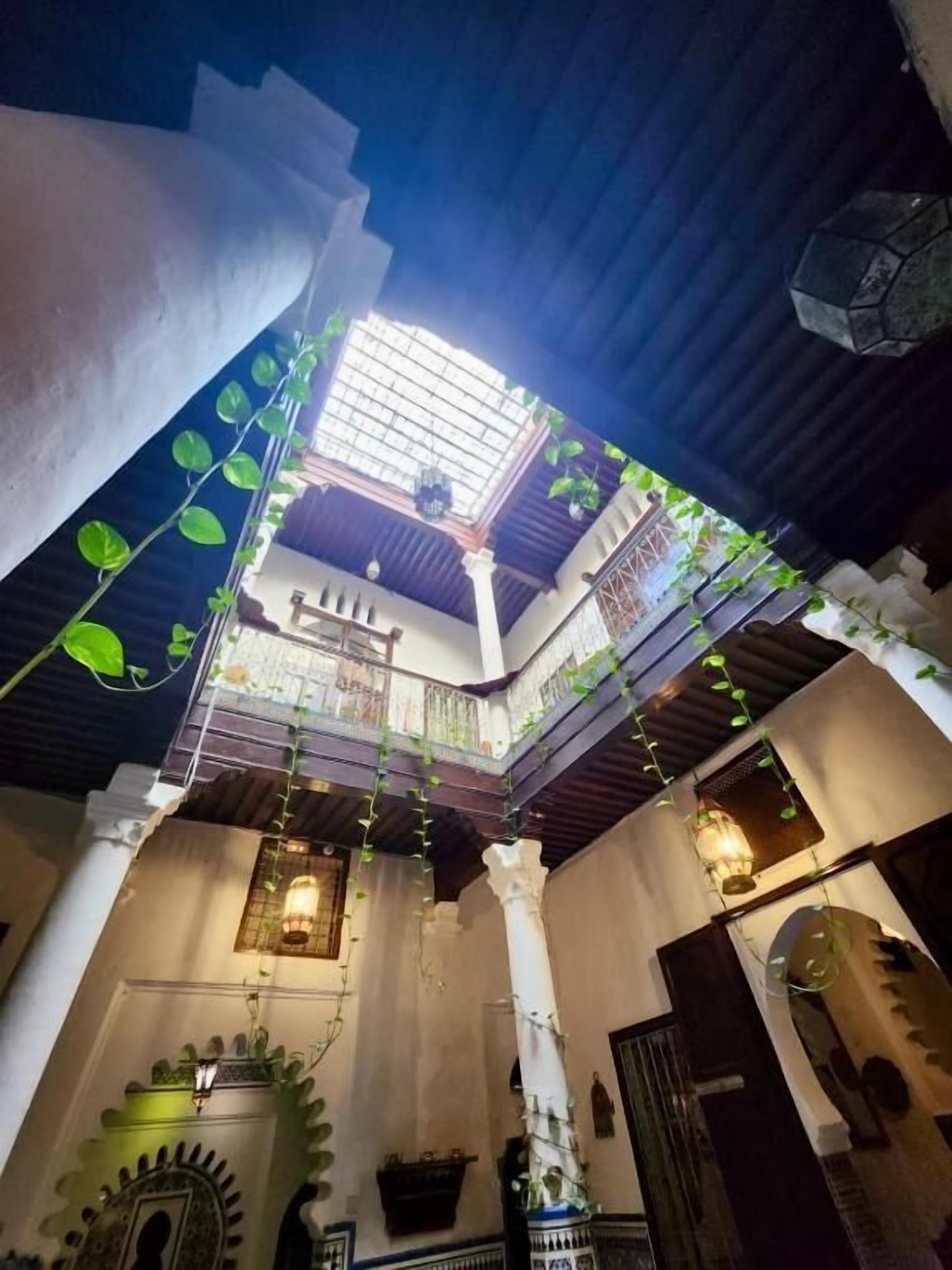 Un patio interior con espacio abierto en el centro, columnas y plantas colgantes.