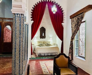 Quarto com cama, uma cadeira e janela com detalhes em ferro.