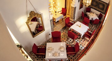 Un comedor con mesas dispuestas para cuatro, sillas tapizadas en rojo, suelo estampado y un espejo decorativo en la pared.