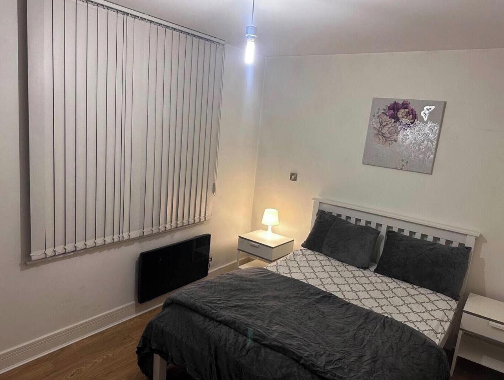Ein Schlafzimmer mit Bett, Nachttisch, Lampe, Heizkörper und Wandbild.
