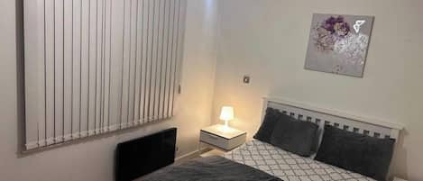 Una camera da letto con un letto, un comodino, una lampada, un termosifone e un'opera d'arte appesa al muro.