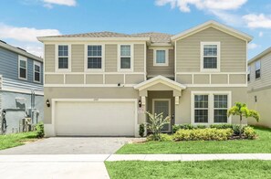 A two-story residential building with a garage, a front door, and a small front yard with landscaping. - Luxury 10BR Windsor Island Villa | 24 | Private Pool | Spa | Game Room |Theater (Davenport)