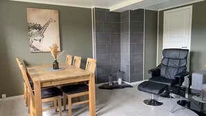 A dining area with a wooden table and chairs, a black leather chair, and a grey tiled wall.