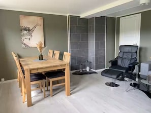 A dining area with a wooden table and chairs, a black leather chair, and a grey tiled wall.