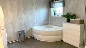 A bathroom with a freestanding bathtub, a window with a curtain, a potted plant, and a laundry basket.