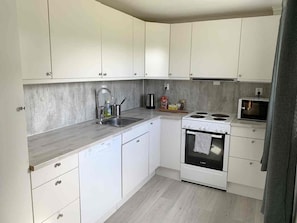 A modern kitchen with white cabinets, a stainless steel sink, a Bosch oven, and a microwave.