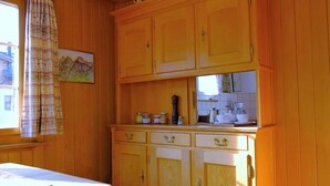 A kitchen with wooden cabinets, a window with a curtain, and a painting on the wall. - Lill Britta 2, mittlere Wohunug Appartement/Fewo, Dusche und Bad, WC, Komfort by Interhome (Arosa)