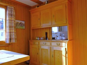 A kitchen with wooden cabinets, a window with a curtain, and a painting on the wall. - Lill Britta 2, mittlere Wohunug Appartement/Fewo, Dusche und Bad, WC, Komfort by Interhome (Arosa)