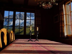 A dining area with a table set for two, a view of mountains through large windows, and a chandelier. - Lill Britta 2, mittlere Wohunug Appartement/Fewo, Dusche und Bad, WC, Komfort by Interhome (Arosa)