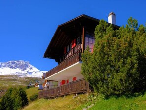 A two-story chalet with a balcony, surrounded by greenery and a mountain backdrop. - Lill Britta 2, mittlere Wohunug Appartement/Fewo, Dusche und Bad, WC, Komfort by Interhome (Arosa)
