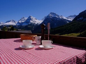 Ein Tisch mit Tassen, Untertassen, einem Korb und einem Gewürzmühlen auf einer karierten Tischdecke, mit Bergelandschaft im Hintergrund.