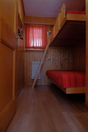 A wooden interior with a bunk bed, a radiator, and a window with patterned curtains. - Lill Britta 2, mittlere Wohunug Appartement/Fewo, Dusche und Bad, WC, Komfort by Interhome (Arosa)