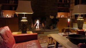 A cozy living room with a fireplace, leather sofa, and bookshelves. - Lill Britta 2, mittlere Wohunug Appartement/Fewo, Dusche und Bad, WC, Komfort by Interhome (Arosa)