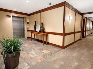 Un vestíbul d'hotel amb una recepció, un rellotge, un vas i una planta en test.