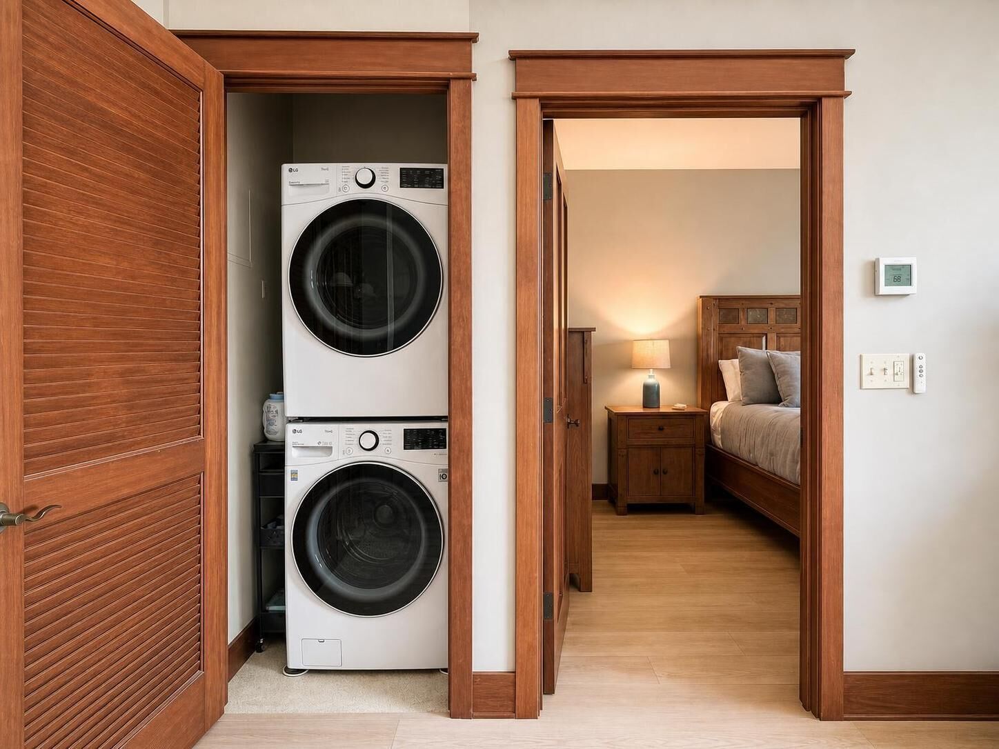 Un cuarto de lavandería con dos lavadoras apiladas y un dormitorio con cama, mesita de noche y lámpara.