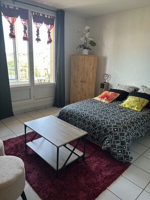 Ein Schlafzimmer mit einem Bett, einem kleinen Tisch, einem Schrank und einem Fenster mit Vorhängen.