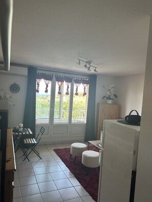 Ein Zimmer mit Esstisch, Stühlen, einem kleinen Teppich, einem Schrank und einem Fenster mit Vorhängen.