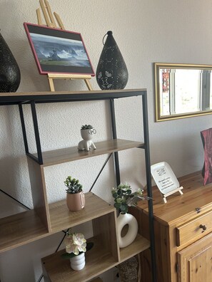 Uma prateleira de madeira com diversos objetos decorativos, incluindo uma moldura, um vaso preto e plantas em vasos.
