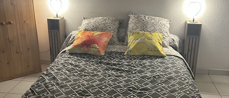A bed with a patterned bedspread, two pillows, two bedside lamps, and a wooden wardrobe.