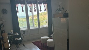 A kitchen with a refrigerator, a dining table with chairs, and a view through the window. - Bright, air-conditioned studio with views of the sea and mountains, 5 minutes from the harbor and downtown. (Port-Vendres)