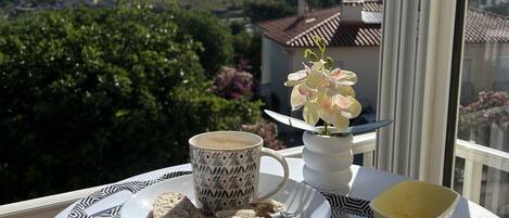 A tray with a cup, pastries, and a flower on a balcony overlooking a scenic view.