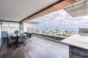 Ein moderner Balkon mit Essplatz, Blick auf eine Stadtlandschaft und blauem Himmel.