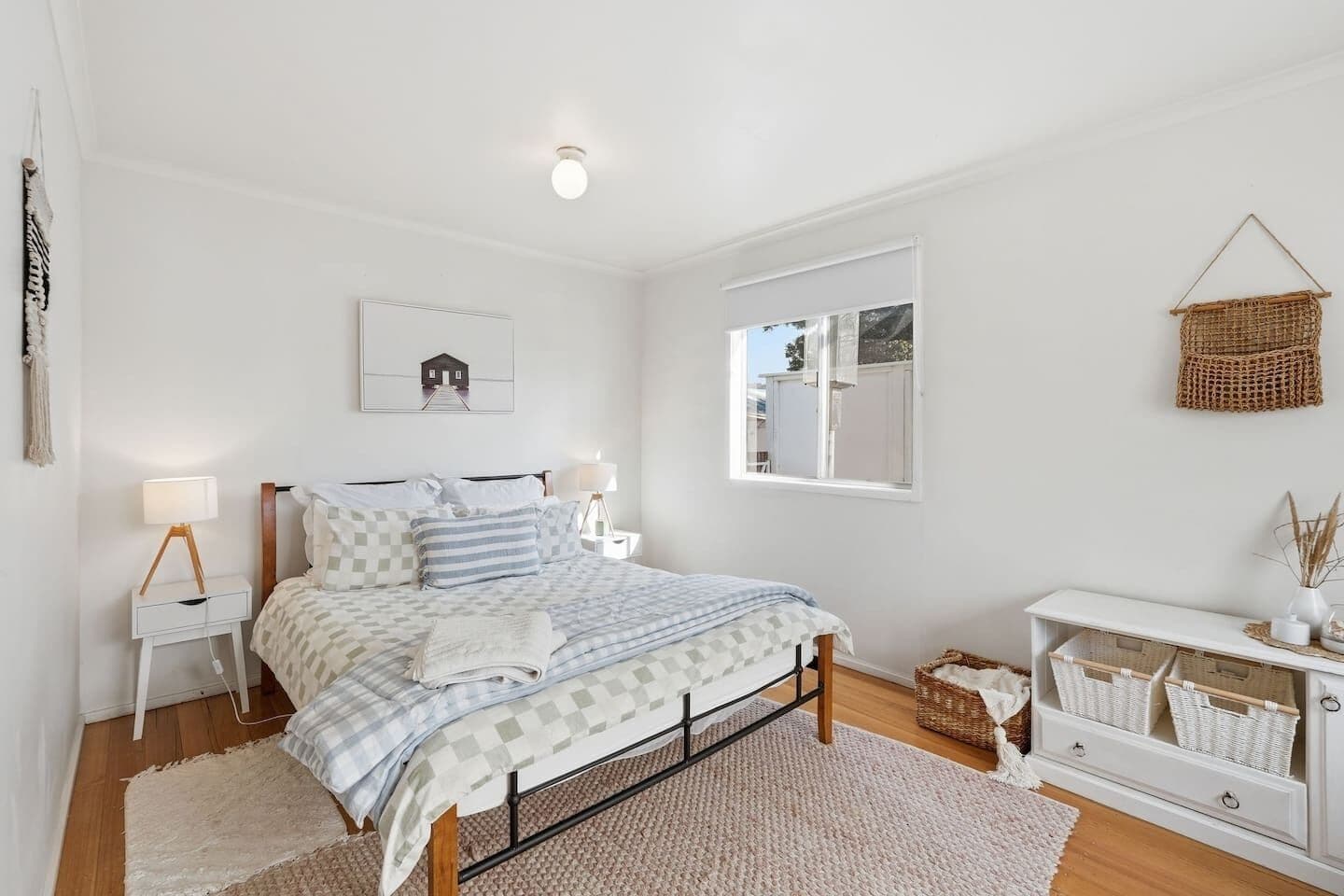 A bedroom with a bed, bedside tables, a window, and a white dresser with baskets.