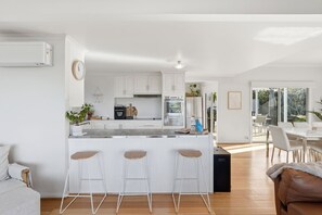A modern kitchen with a central island, bar stools, and a dining area with a table and chairs. - Seven Mile Beach Holiday Home - unwind and restore (Seven Mile Beach)