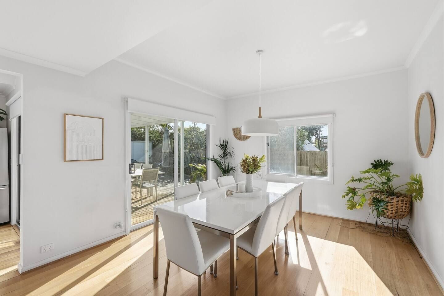 A modern dining area with a white table and chairs, a pendant light, and a view of the outdoors through large windows.
