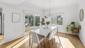 Un'elegante sala da pranzo moderna con un tavolo e sedie bianchi, una lampada a sospensione e vista all'esterno attraverso ampie finestre.
