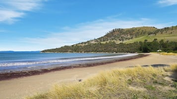 A beach with a clear view of the ocean and a hilly landscape in the background.
