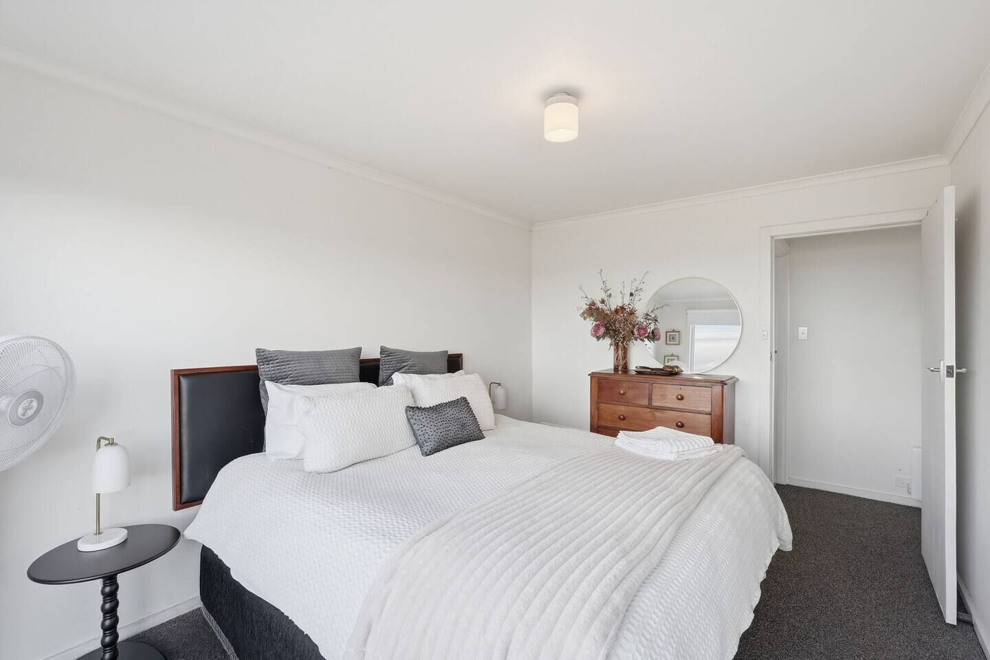A hotel room with a bed, bedside table, lamp, dresser, mirror, and a door.