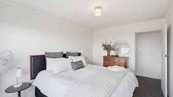 A hotel room with a bed, bedside table, lamp, dresser, mirror, and a door.