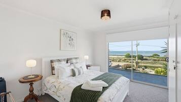 A bedroom with a bed, a bedside table, a lamp, a framed picture, and a view of the outdoors.