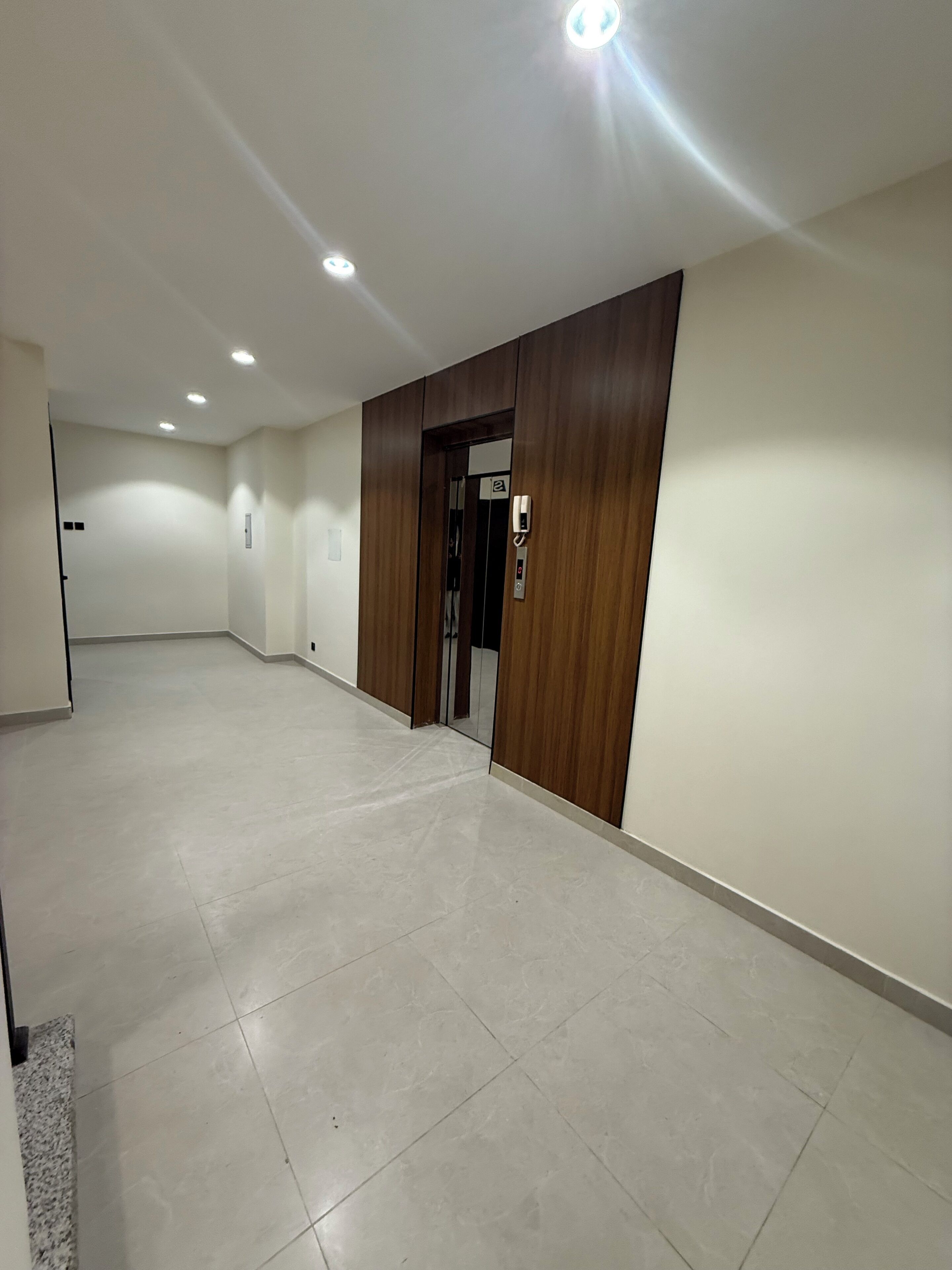 A spacious, well-lit hallway with a wooden door and a visible elevator control panel.
