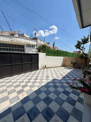 A courtyard with a checkered floor, a black gate, and a green hedge.