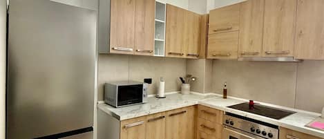 Una cocina moderna con un refrigerador de acero inoxidable, un microondas, un horno, armarios de madera y una encimera de mármol.
