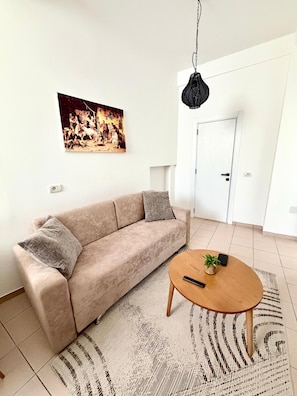 A living room with a beige sofa, a round wooden coffee table, a hanging light fixture, and a wall-mounted painting. - Private apartment with a parking space (Tiranë)