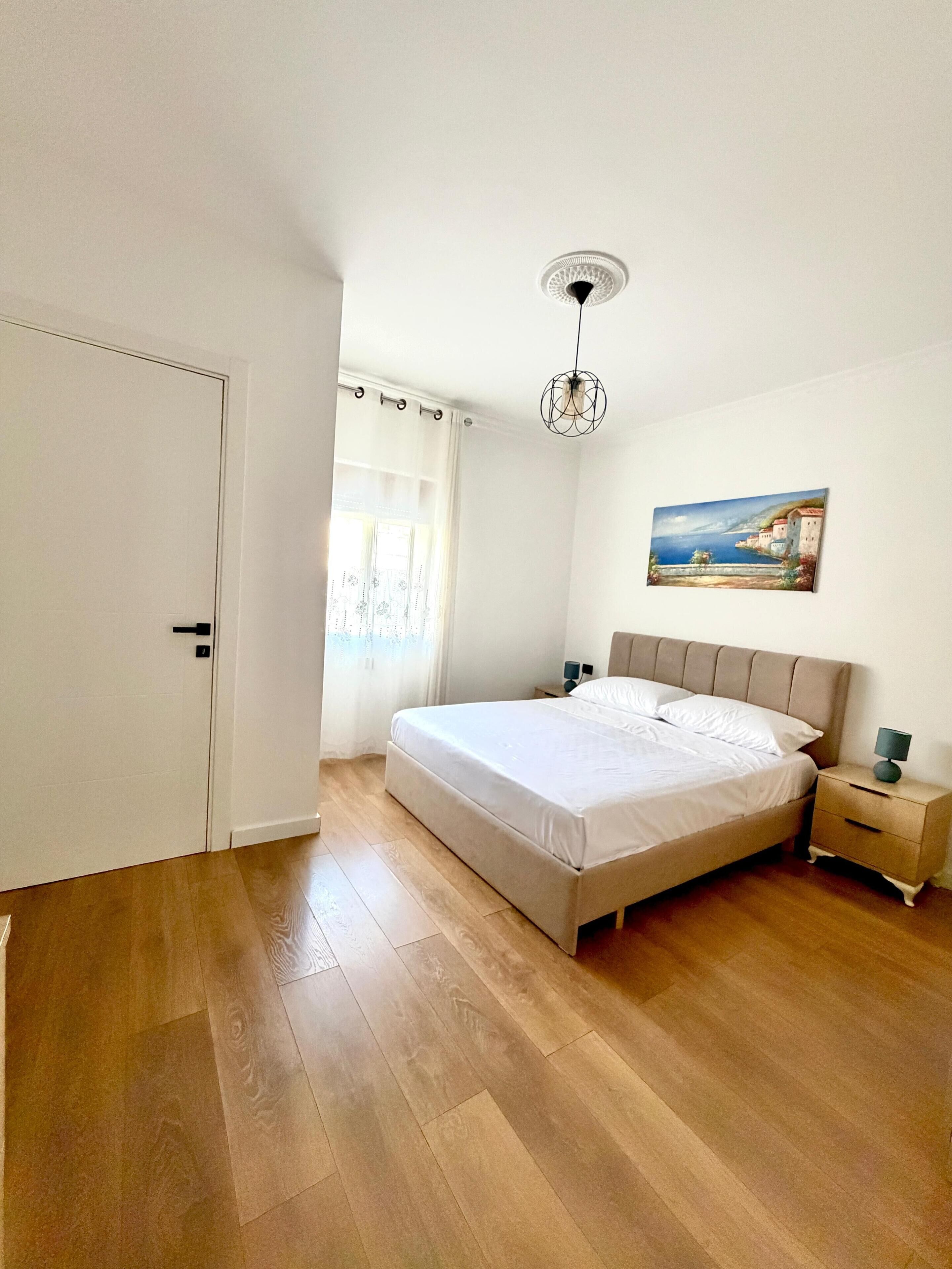 A bedroom with a bed, a nightstand, a lamp, a painting, and a door.