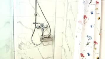 Eine Dusche mit Handbrause und Wandarmatur, ein Duschvorhang mit floralem Muster und ein gefliester Boden mit Marmoroptik.