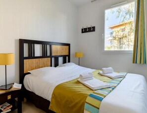 Quarto de hotel com cama, abajures, janela com cortinas e vista para edifícios.