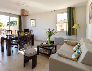 Uma sala de estar com um sofá, uma mesa de jantar com cadeiras, uma mesa de centro e uma janela com cortinas.