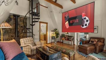 A spacious living room with a high ceiling, a staircase, and a large flat-screen TV displaying the Netflix logo.
