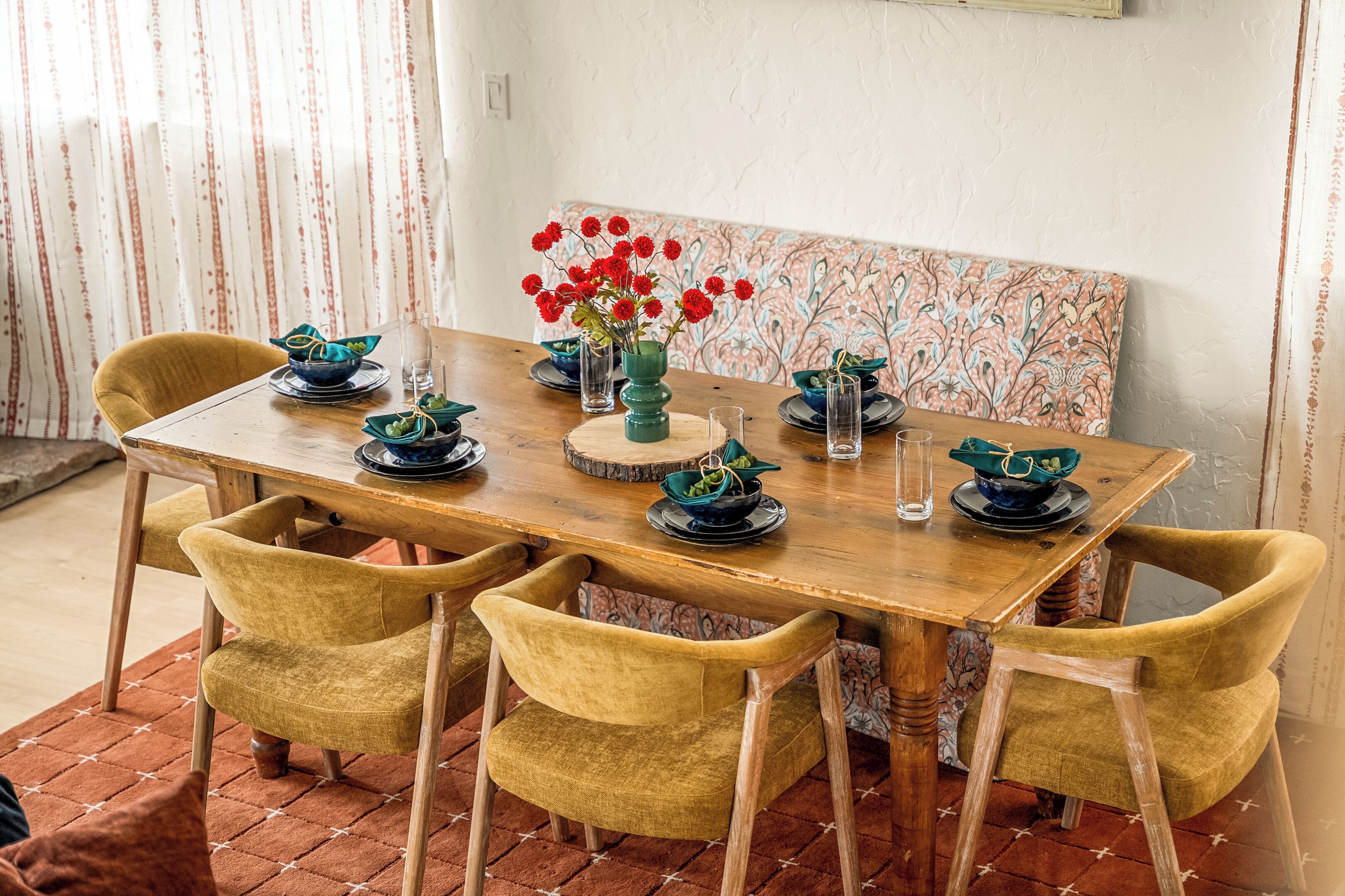 Een eettafel met zes stoelen, een vaas met rode bloemen en verschillende borden en glazen op de tafel.