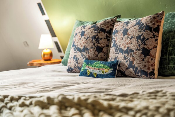 Un letto con una coperta bianca, un cuscino verde e un cuscino blu con motivo floreale.