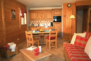 A cozy cabin interior with wooden walls, a dining area, a kitchen with a microwave, and a living area with a sofa.