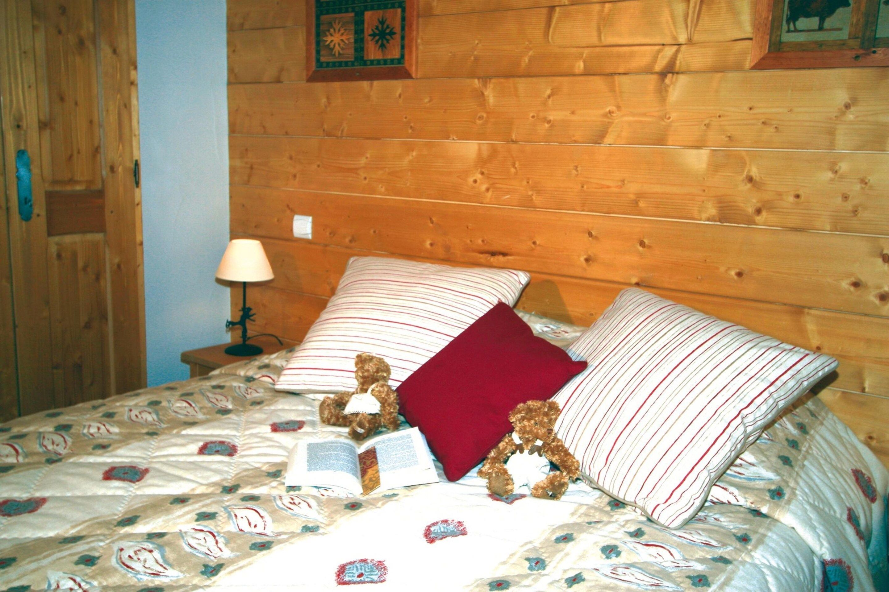 A wooden cabin room with a bed, pillows, a lamp, and a teddy bear.