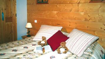 A wooden cabin room with a bed, pillows, a lamp, and a teddy bear.