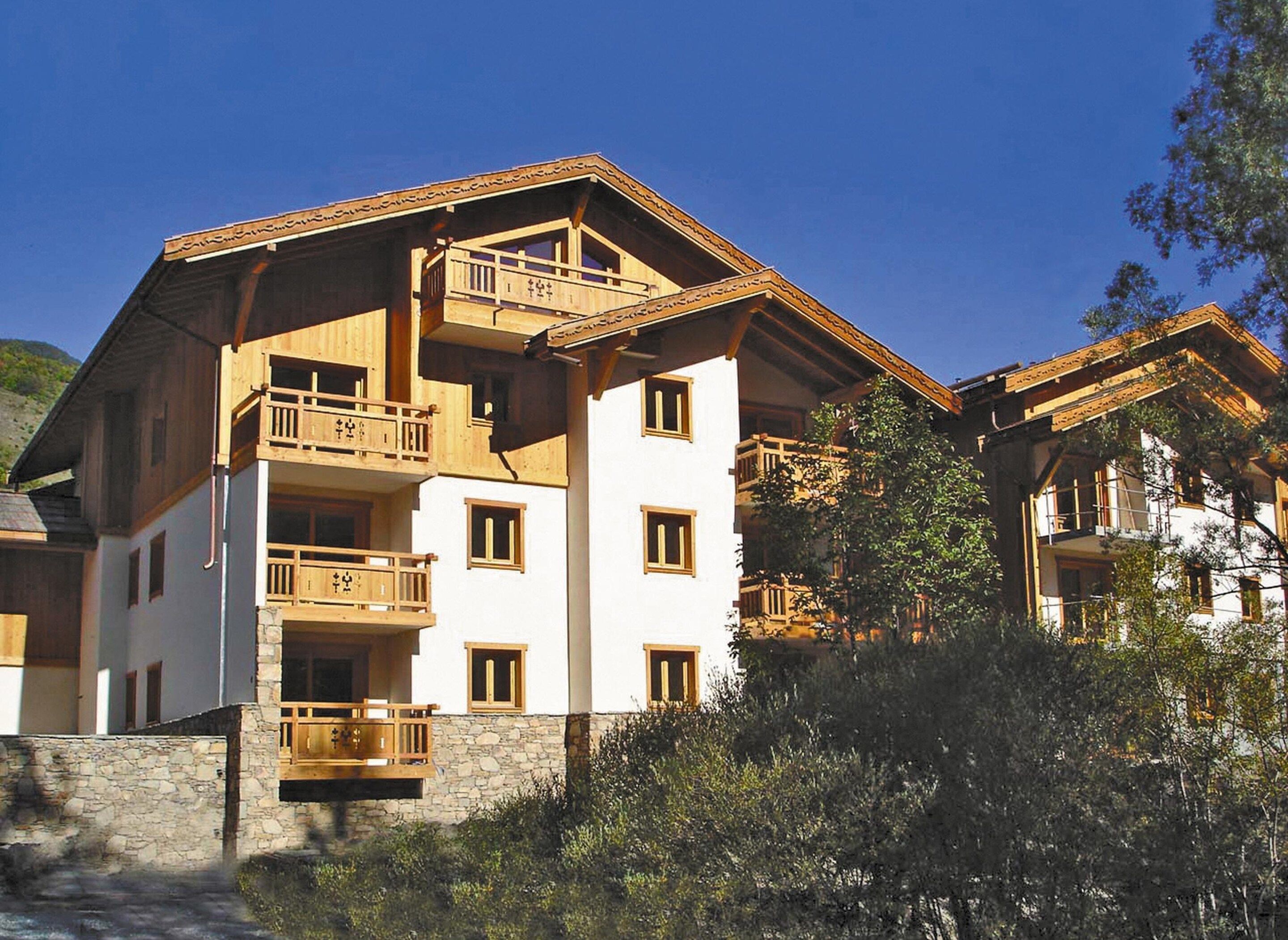 A multi-story building with balconies, stone foundation, and a mountainous backdrop.